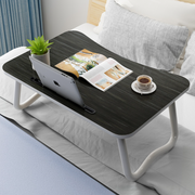Black wooden portable laptop desk with tablet, magazine, and coffee on a bed.