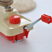 Manual red and cream hand-cranked kitchen grinder tool on a white background.