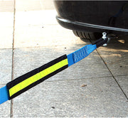 Blue heavy-duty tow strap attached to the rear of a black car on a paved surface