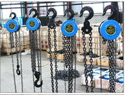 Six industrial manual chain hoists hanging in a warehouse setting.