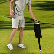 A person walking on a green golf course holding a black golf club head cover.