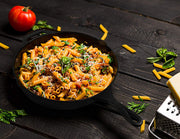 Penne pasta with tomato sauce and fresh basil in a black cast iron skillet on a dark wooden table