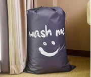 Dark grey laundry bag with white wash me text and smiley face design.