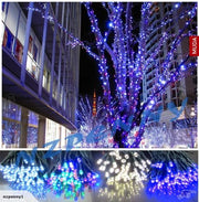 Blue and multi-color LED fairy lights decorating trees and urban buildings at night.